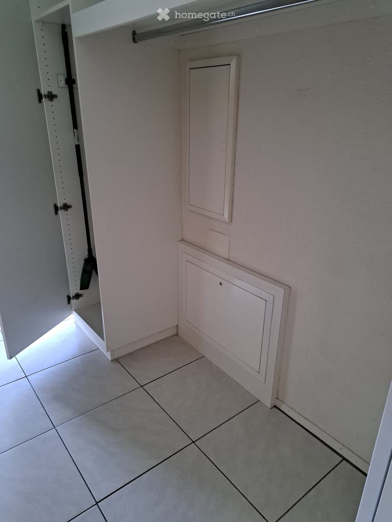 Empty closet with white tiled floor and built-in storage units, featuring a sliding door and a small electrical panel.