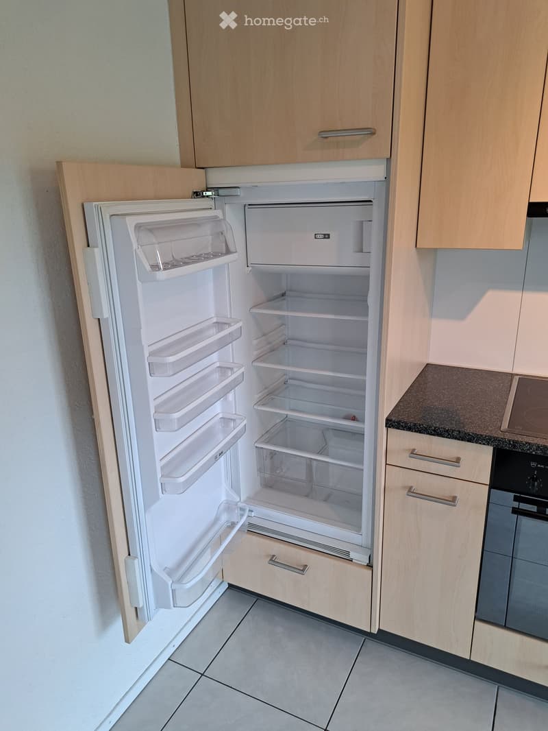 Modern kitchen with light wooden cabinets, a white refrigerator with multiple shelves and drawers, and a tiled floor.