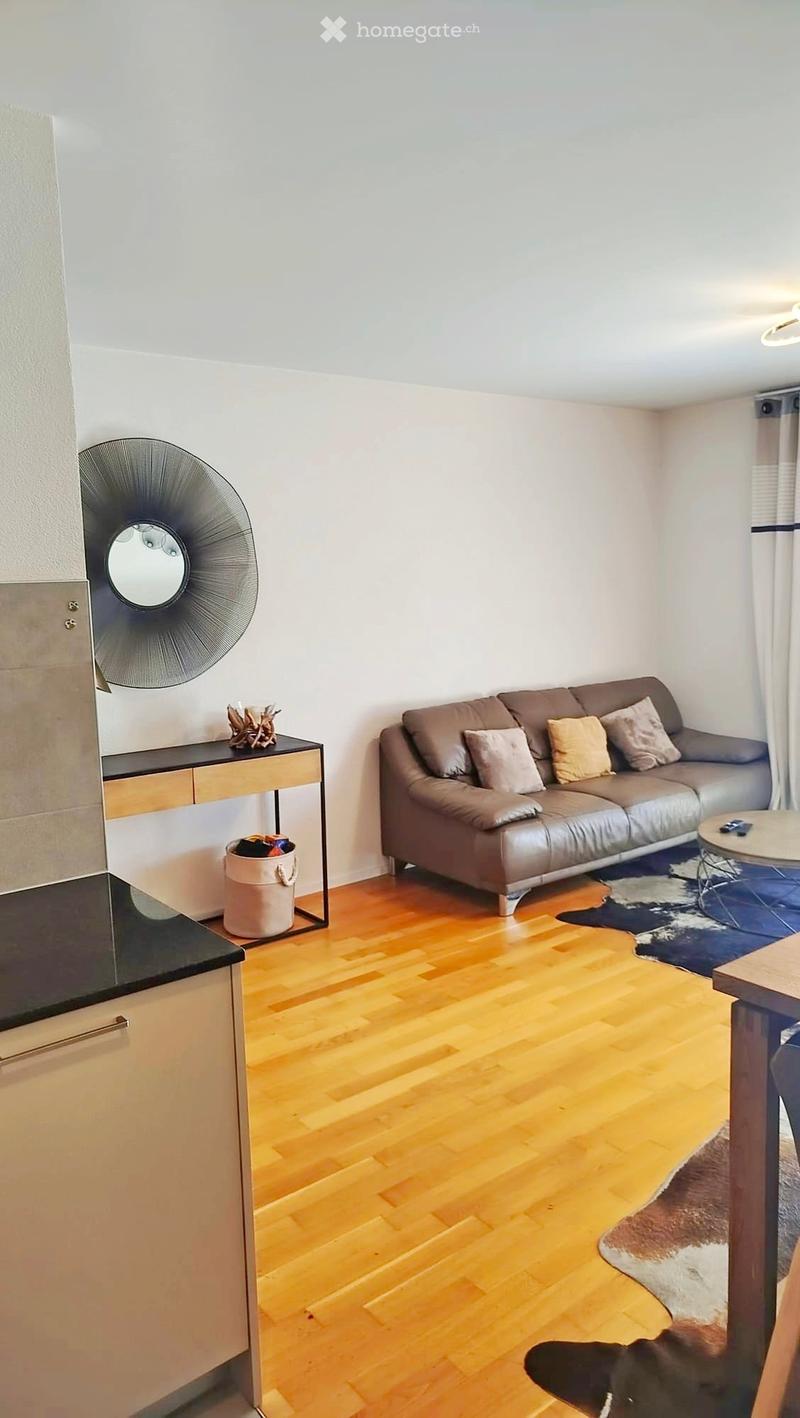 Modern living room with wooden flooring, a brown leather sofa, a coffee table, a decorative mirror, and a small table with a decorative item on it.