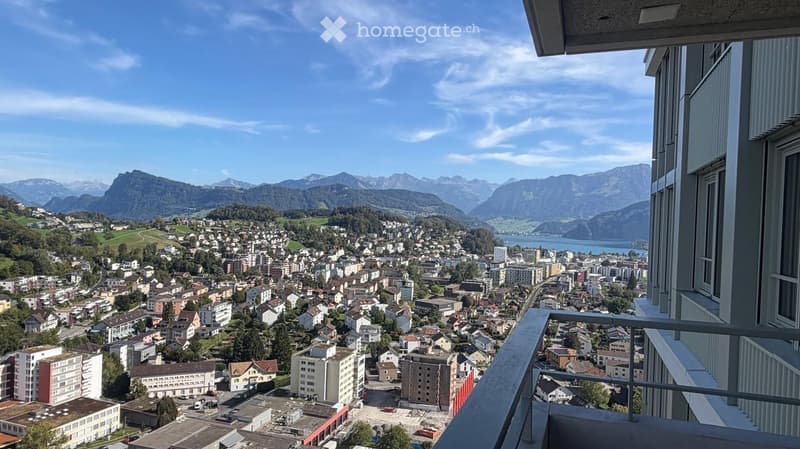Balcony with panoramic view of a town, surrounded by mountains and a lake.