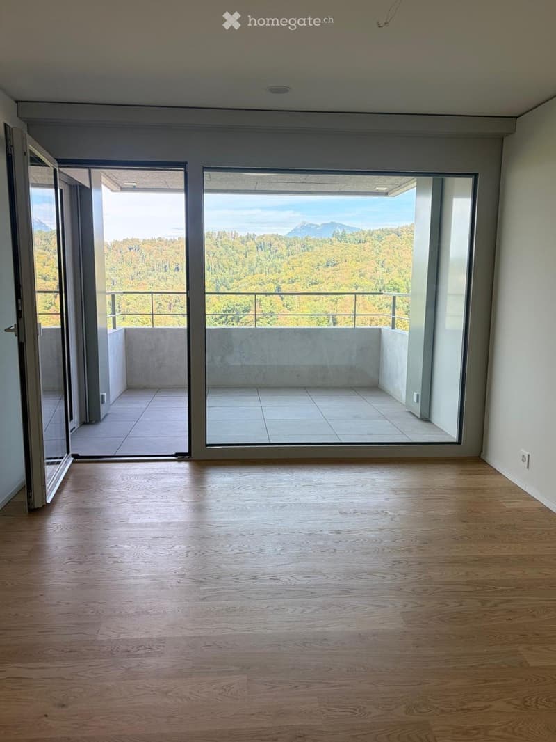 Empty room with wooden flooring, large sliding glass doors leading to a balcony with scenic mountain and forest views.