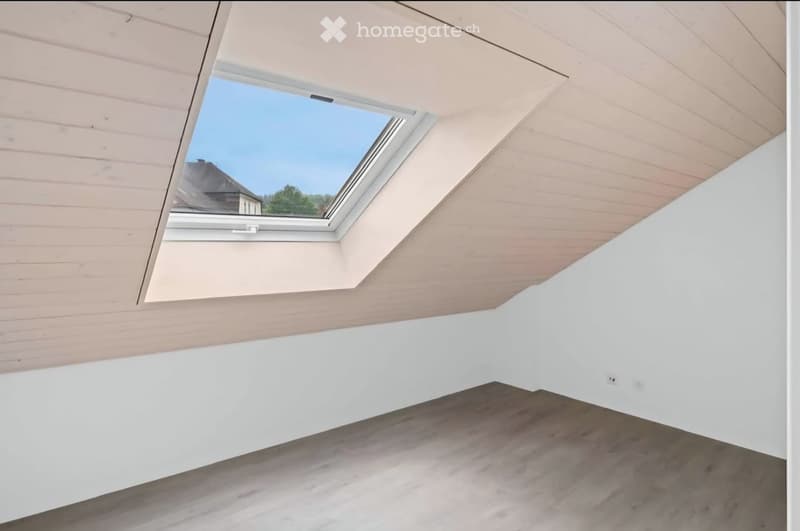 Empty attic space with wooden slatted ceiling, white walls, concrete floor, and a skylight window offering a view of the outdoors.