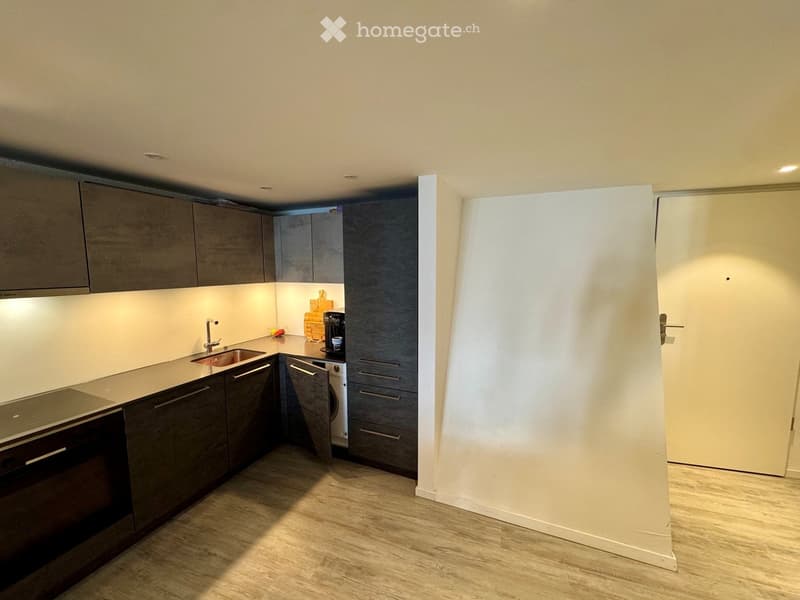 Modern kitchen with dark grey cabinets, light countertops, and built-in appliances including an oven and washing machine. The space features a sink with a modern faucet and a coffee maker on the counter.