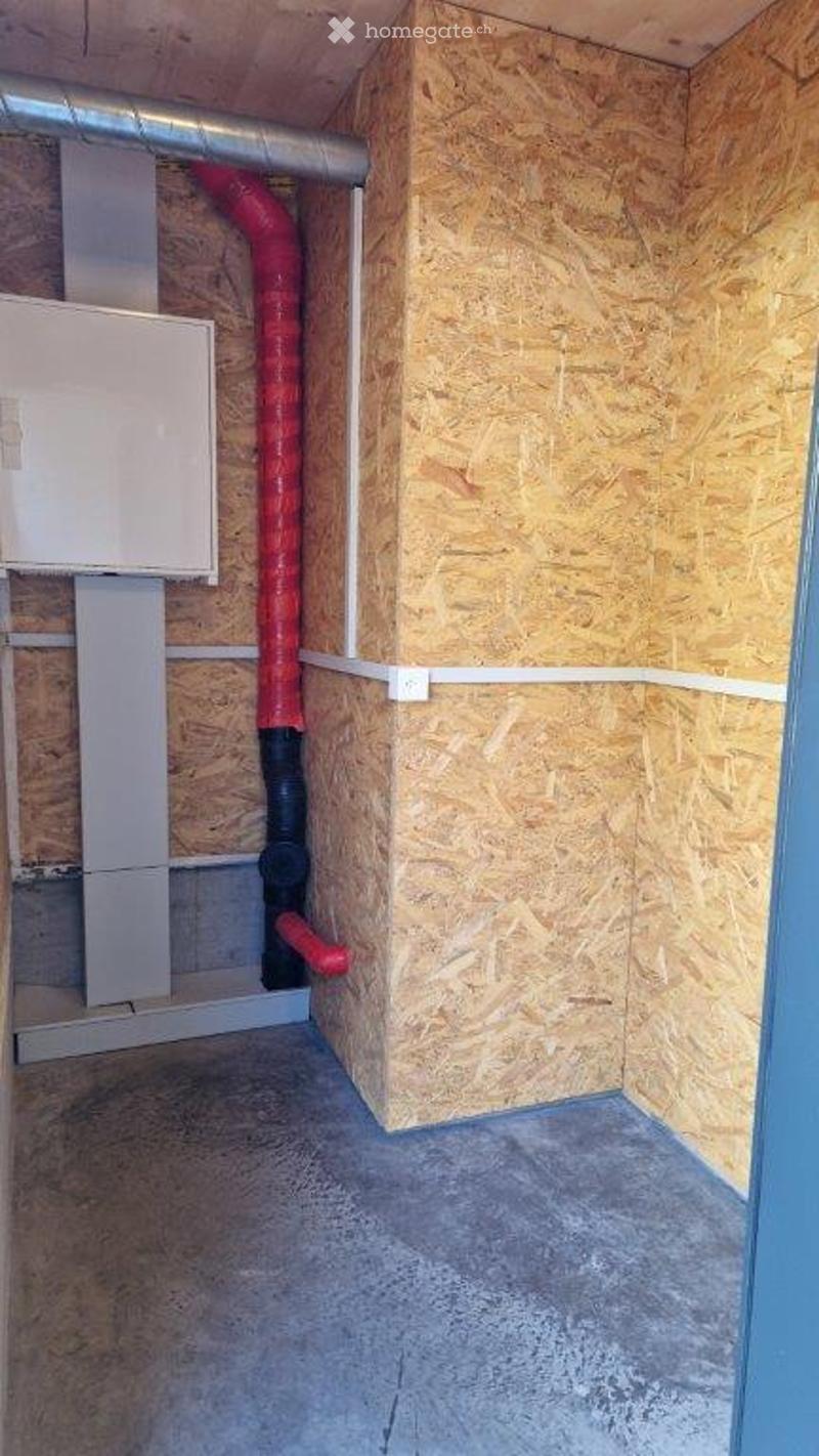 Empty utility room with exposed wooden panel walls, concrete floor, and visible red and black ventilation ducts.