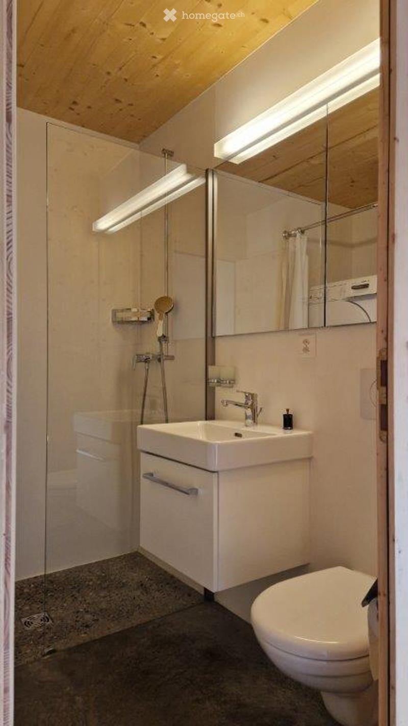 Modern bathroom with a white sink, mirror, toilet, and glass-enclosed shower. Features sleek fixtures and warm lighting.