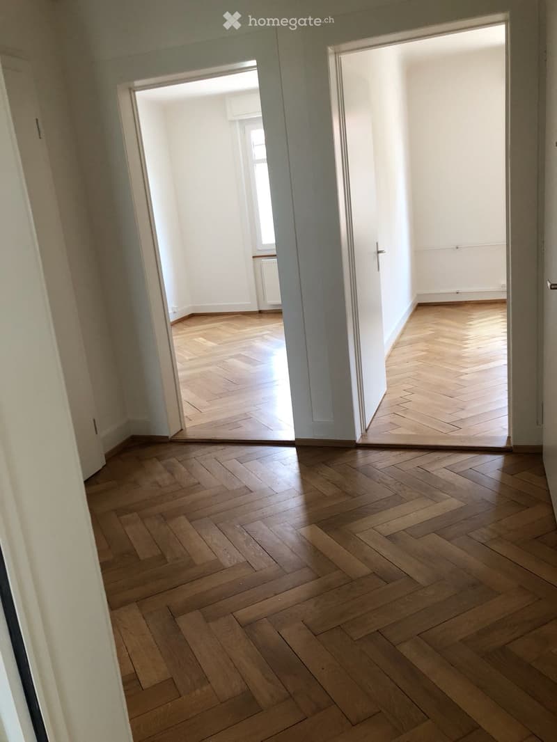 Empty hallway with wooden flooring and white walls, featuring open doors leading to adjacent rooms.