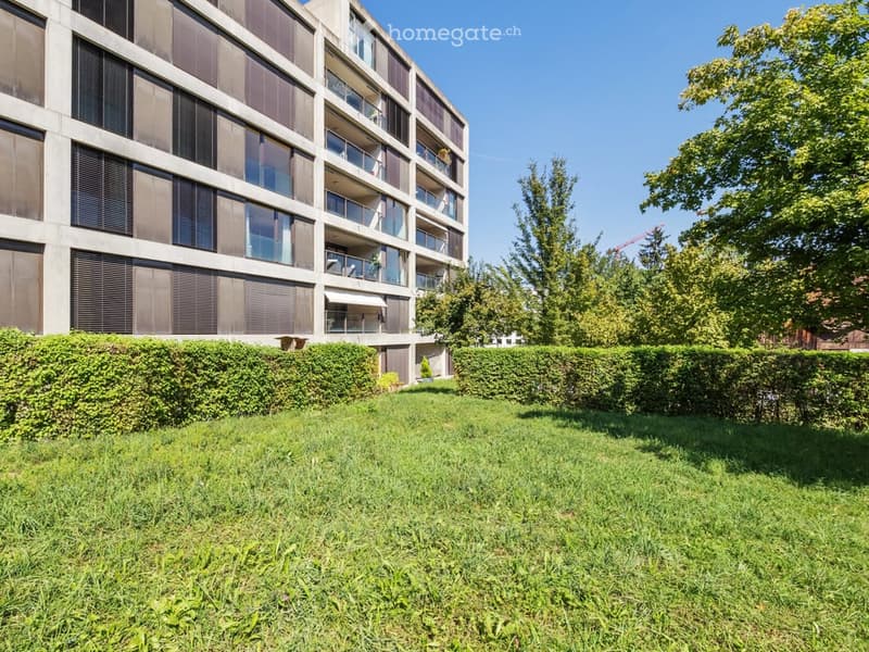 Well-maintained lawn in front of a modern multi-story apartment building with balconies and large windows.