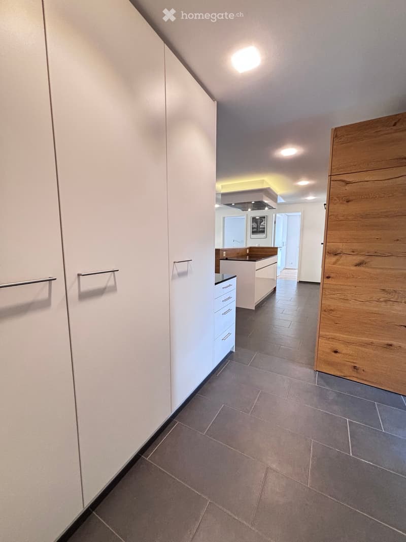 Empty room with white wardrobes, black tiled floor, kitchen, wooden door
