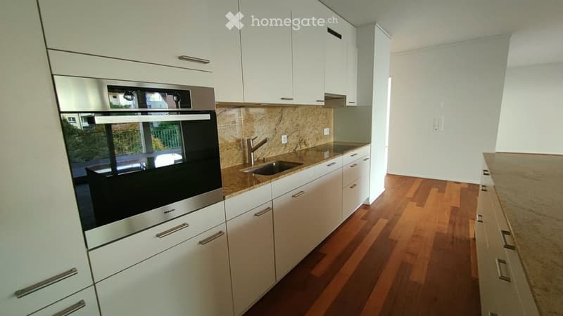Modern kitchen with white cabinets, stainless steel oven, granite countertop, and wooden flooring.