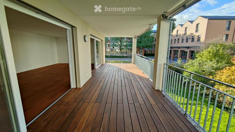 Balcony with wooden decking, metal railing, and open sliding doors leading to the interior.