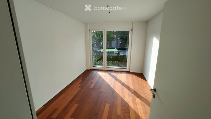 Empty room with wooden flooring and white walls, featuring a large glass door leading to an outdoor area.