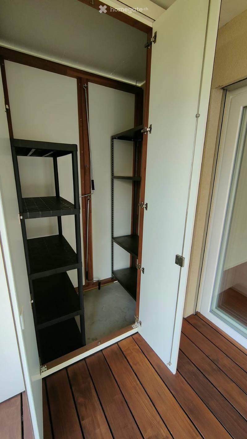 Empty room with wooden flooring, white walls, and a partially open closet with empty shelves.