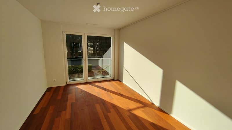 Empty room with wooden flooring, large glass sliding doors leading to a balcony, and natural light streaming in.