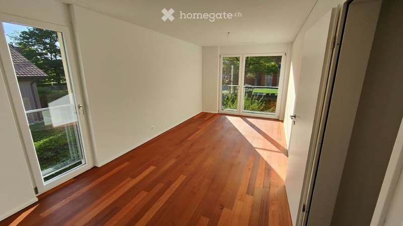 Empty room with wooden flooring, white walls, and large glass doors leading to an outdoor area.