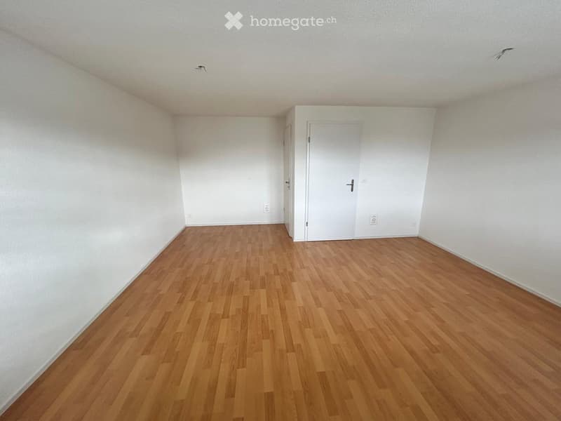 Empty room with wooden flooring and white walls, featuring a closed white door and visible electrical outlets.