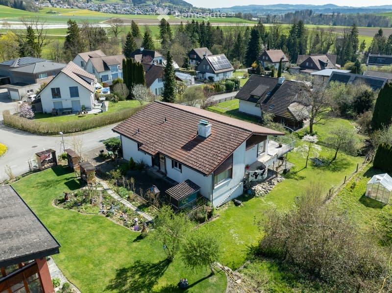 Aerial view of a residential neighborhood with multiple houses, well-maintained gardens, and surrounding greenery.