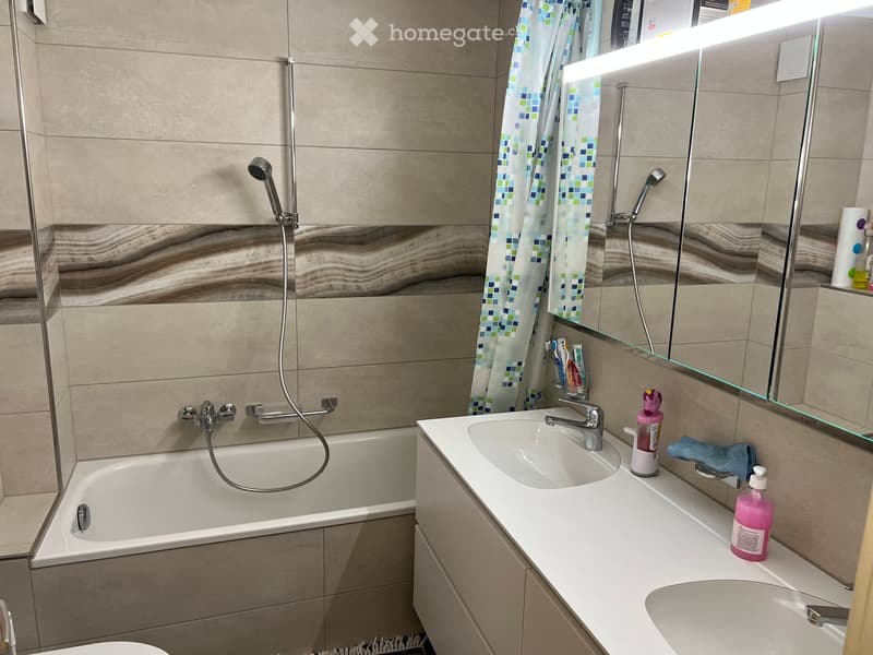 Modern bathroom with a bathtub, double sink, large mirror, and a shower area with a curtain.