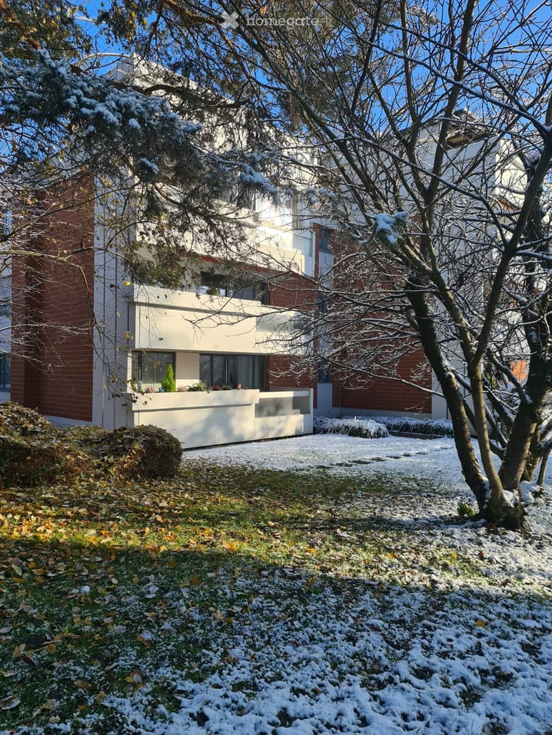 Modern two-story building with white and red brick facade, large windows, and snow-covered ground.