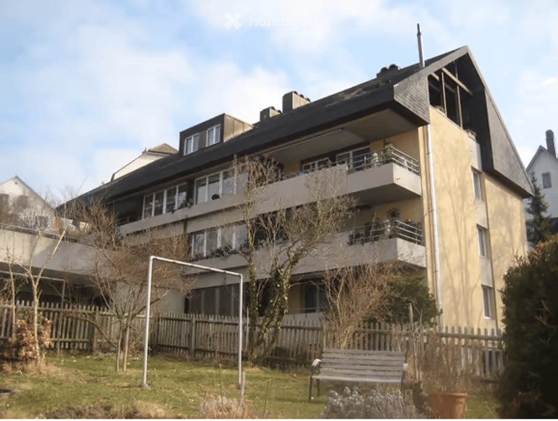 3 story building, yellow walls, balconies, small yard with a bench and a fence