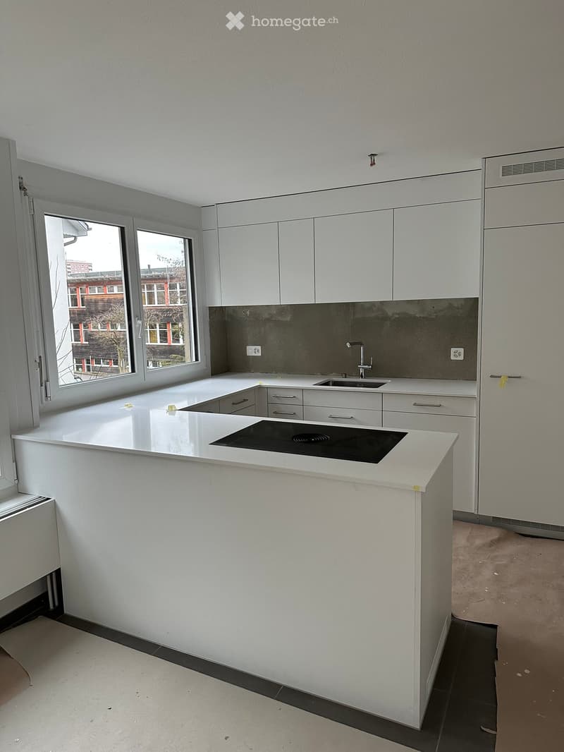 Modern kitchen with white cabinets, a central island with an induction cooktop, and a sink with a faucet. Large windows provide natural light.