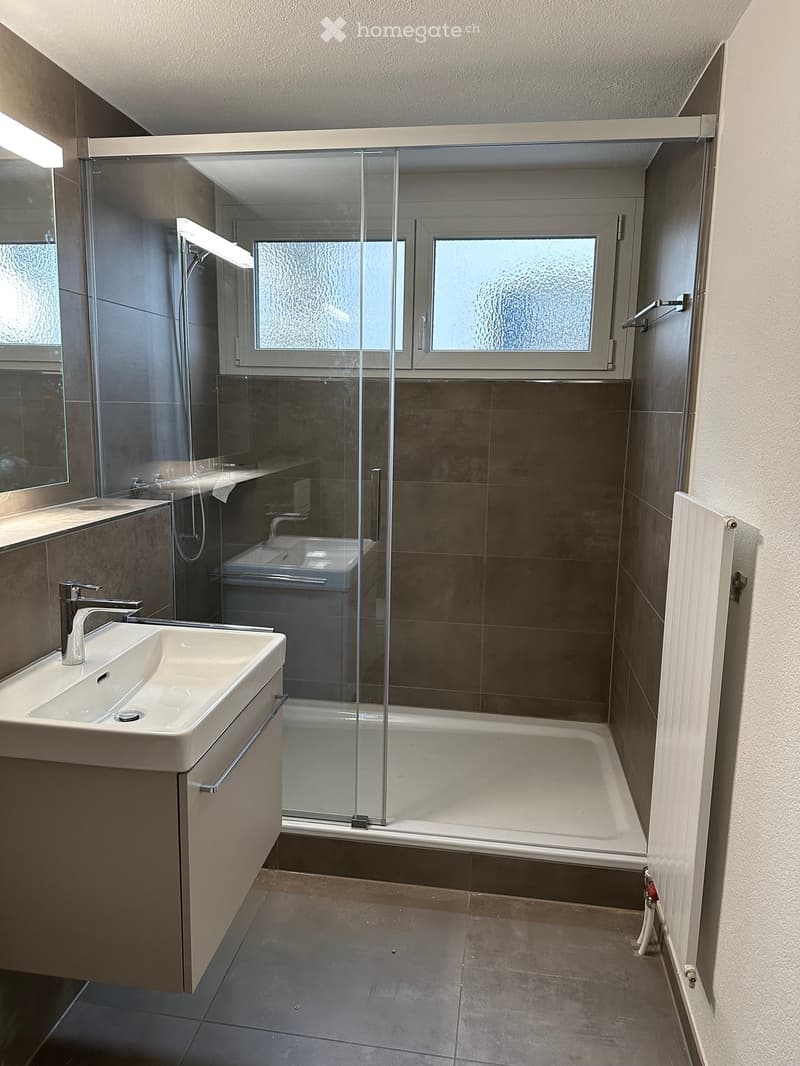 A modern bathroom with a walk-in shower, a sink, a bathtub, and a separate mirror, all set in a tiled wall and floor setting.