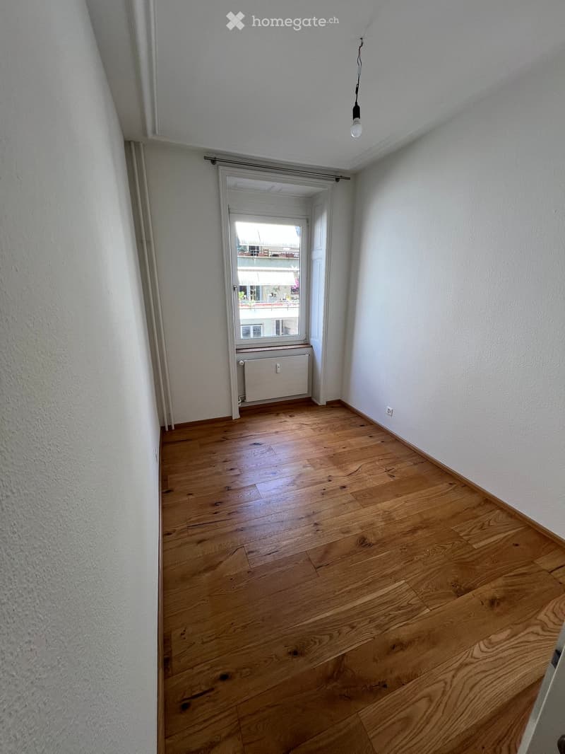 Empty room with wooden flooring, white walls, and a window with a radiator below it.