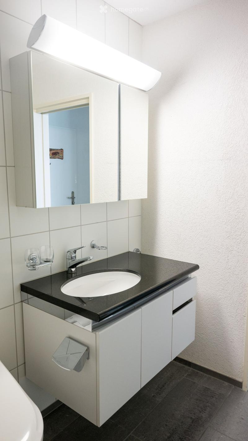 Bathroom with white tiles, black countertop, white sink, silver faucet, white cabinets, mirror, and a toilet.