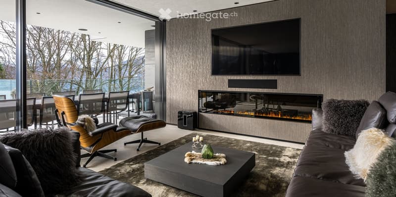 Modern living room with a large fireplace, flat-screen TV, leather sofa, coffee table, and dining area with chairs and table.