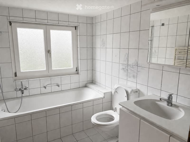 Modern bathroom with white tiled walls and floor, featuring a bathtub, toilet, sink, and mirror.