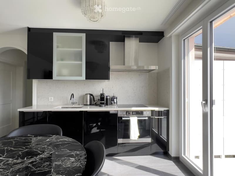 Modern kitchen with black and white cabinets, a marble dining table, and a sleek oven. The space features a large window and a chandelier.