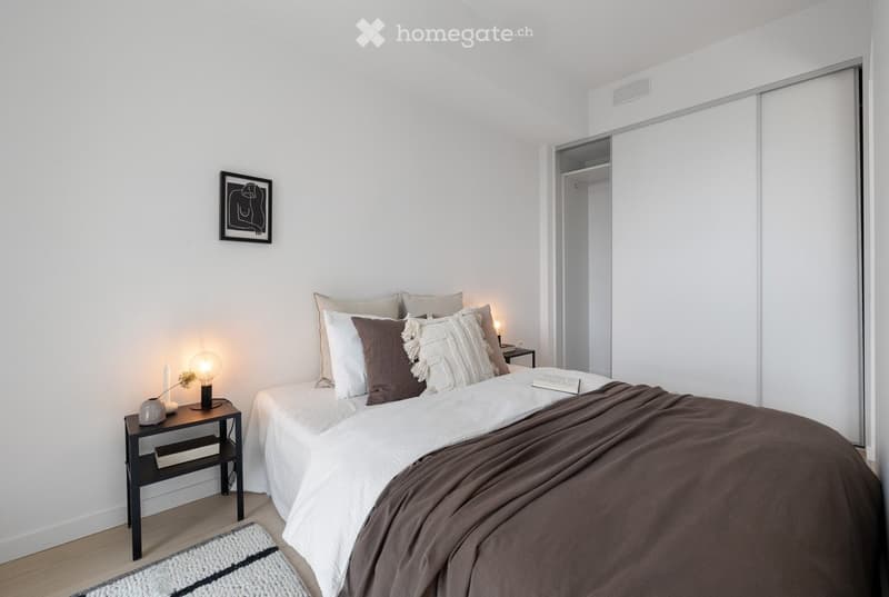 Modern bedroom with a neatly made bed, nightstand, lamp, and a picture frame on the wall.