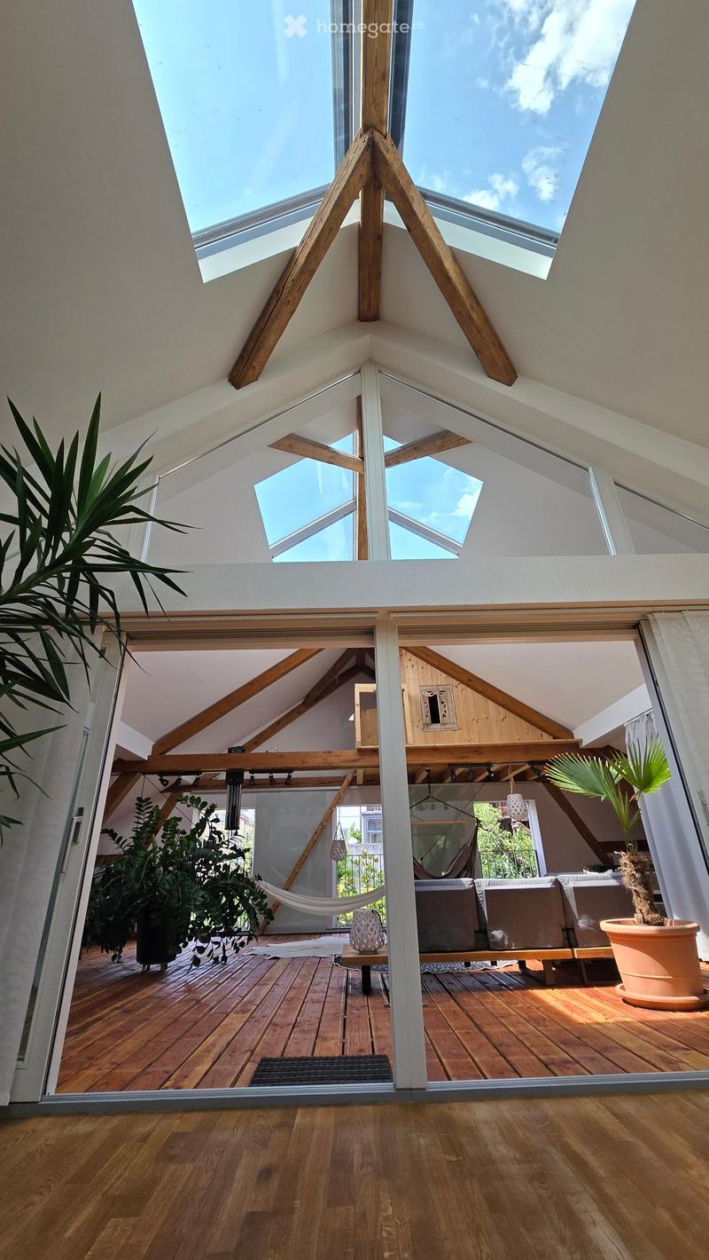 Bright, airy attic space with wooden beams and skylights, featuring a sofa, small table, hammock, and potted plants.