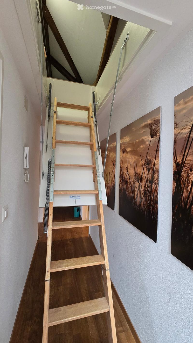 Wooden staircase with white walls, artwork on the right side, and a small blue container at the base of the stairs.