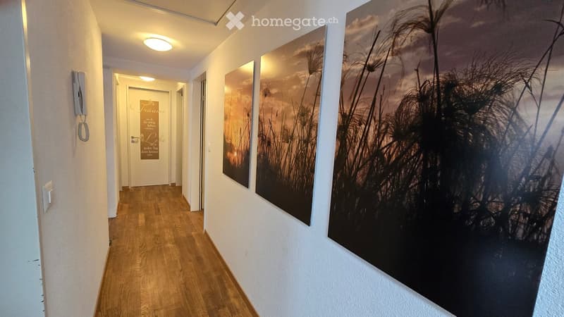A well-lit hallway with wooden flooring, white walls, and large framed artwork depicting a natural scene. A door labeled "Traume" is visible at the end of the corridor.