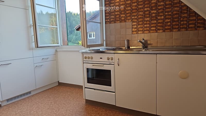 Modern kitchen with white cabinets, a built-in oven, a sink with a faucet, and large windows overlooking a green area.