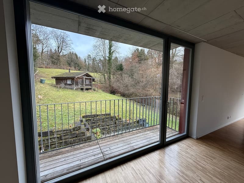 Spacious balcony with wooden decking, metal railing, and scenic view of a grassy hillside and wooden cabin.