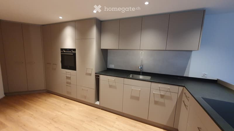 Modern kitchen with light-colored cabinets, black countertops, and a stainless steel sink.