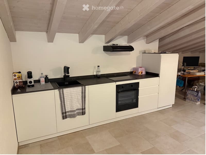 Modern kitchen with white cabinets, black countertops, and stainless steel appliances including a sink, oven, and coffee machine. A towel hangs from the oven handle, and various items are placed on the countertops.