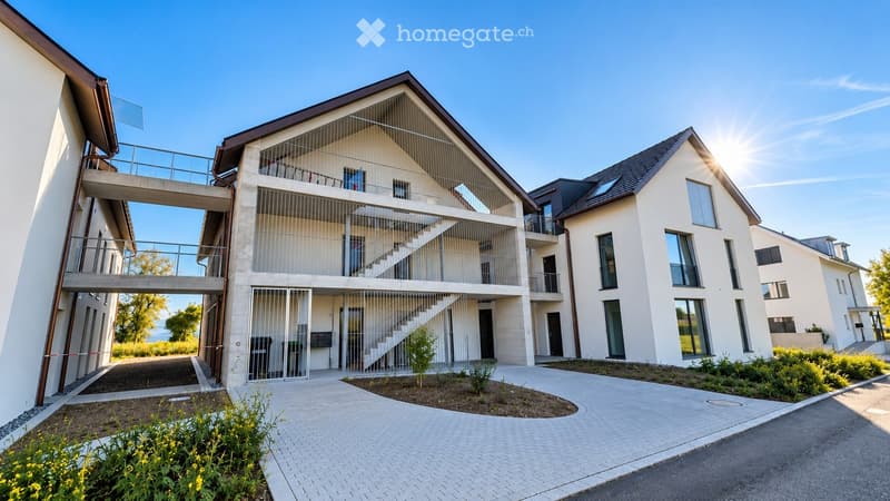 Modern two-story residential building with white walls, large windows, and a staircase leading to a balcony. The entrance features a gated area with small plants and a paved pathway.