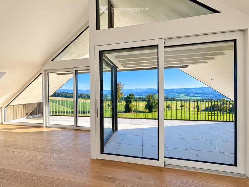 Bright, airy room with large sliding glass doors opening to a tiled balcony, offering scenic views of green fields and distant mountains.
