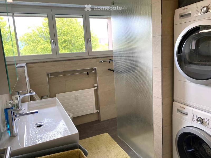 Modern bathroom with a white sink, chrome faucet, Bosch washing machine and dryer, glass shower enclosure, and tiled walls.