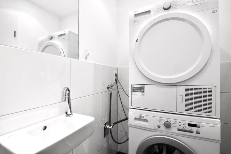 Modern bathroom with a white sink, chrome faucet, and stacked washing machine and dryer unit.
