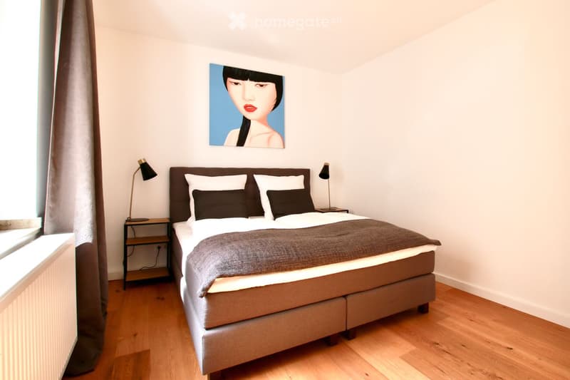 Modern bedroom with a large bed, nightstands, lamps, and a picture on the wall.