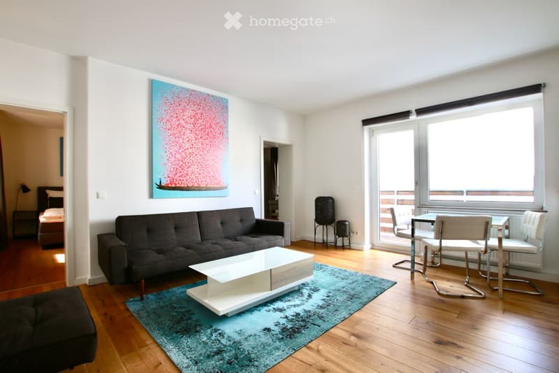 Modern living room with a grey sofa, white coffee table, blue rug, and a balcony with chairs and a table.
