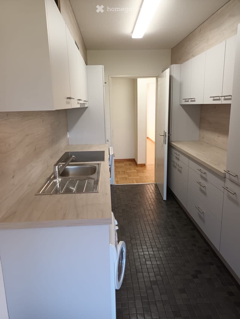 Modern kitchen with white cabinets, wooden countertops, black tiled floor, stainless steel sink, and a visible washing machine.