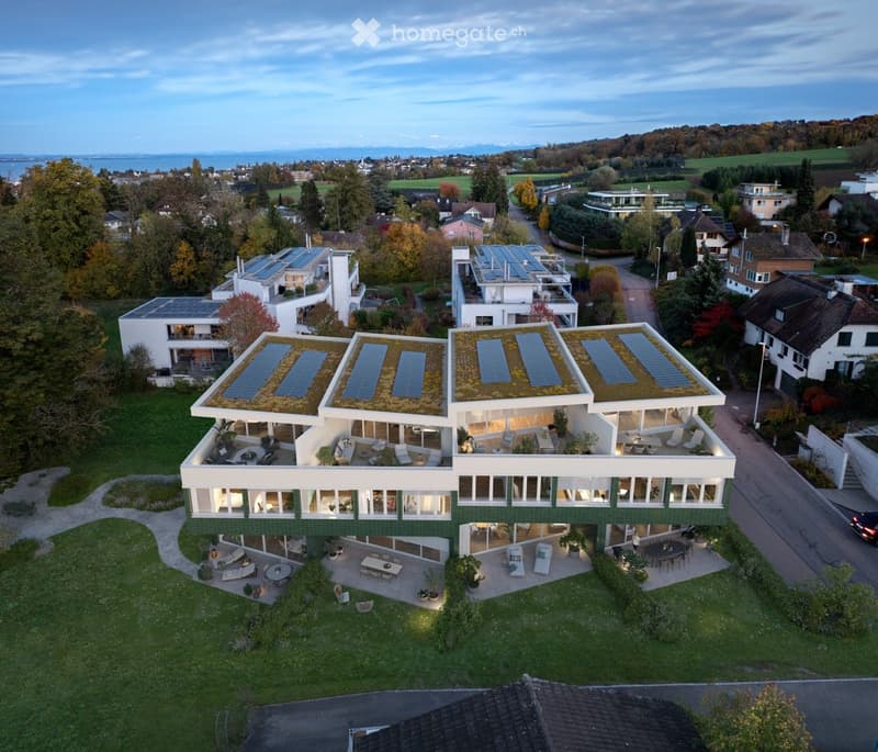 A modern, multi-story house with a green roof and solar panels, surrounded by a well-maintained garden and outdoor seating areas.