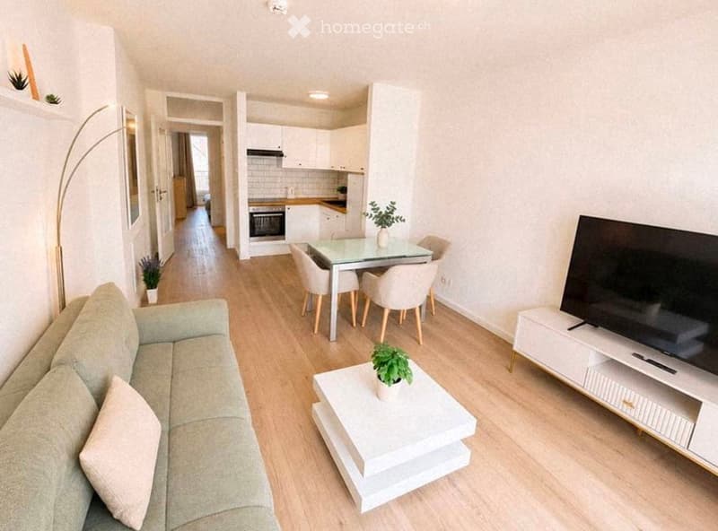 Modern, open-plan living and dining area with light wood flooring, white walls, and contemporary furniture including a sofa, coffee table, TV stand, dining table, and chairs.