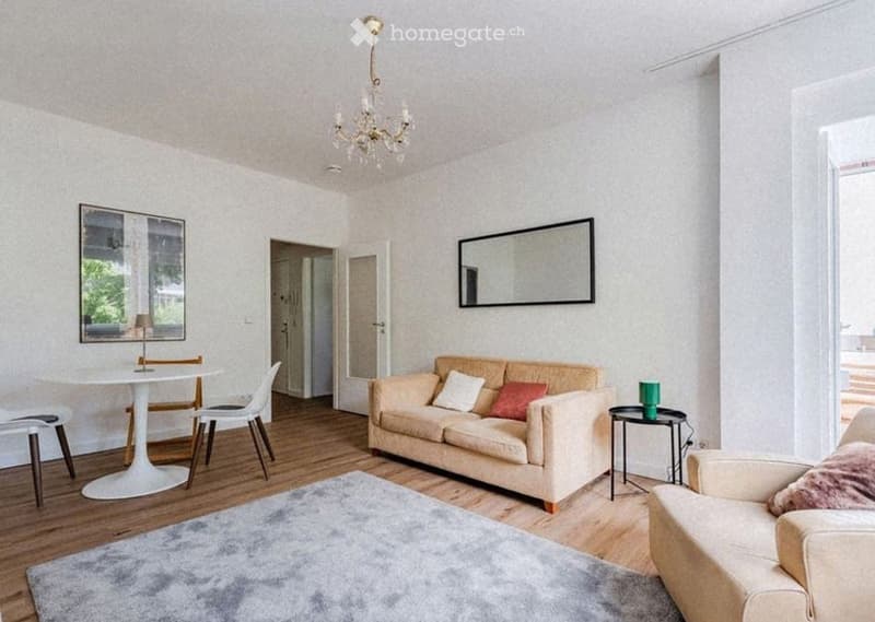 Living room with light-colored sofa, coffee table, dining table, chairs, and a large mirror on the wall.