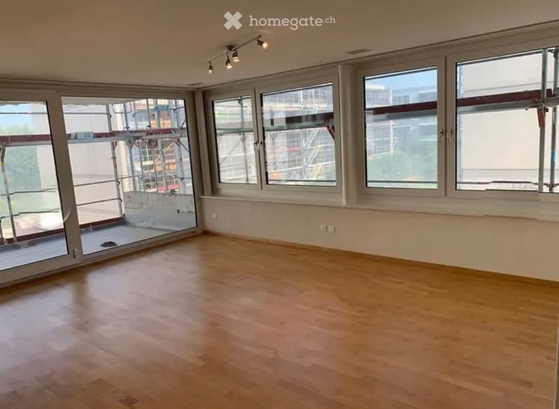 Empty room with wooden flooring, large windows, and track lighting. No furniture or equipment present.
