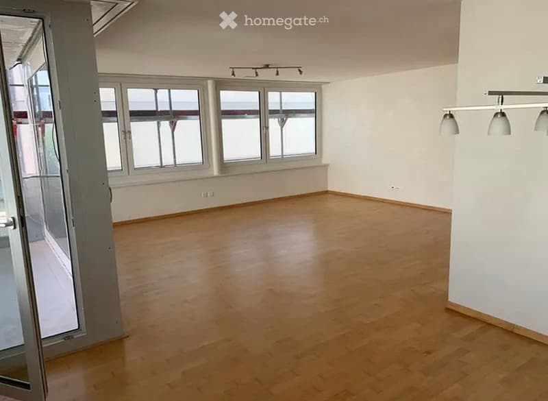 Empty room with wooden flooring, large windows, and modern lighting fixtures.